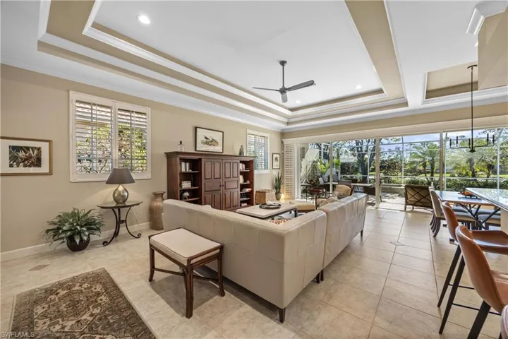 Living room featuring light tile patterned floors, a raised ceiling, ceiling fan, and ornamental molding