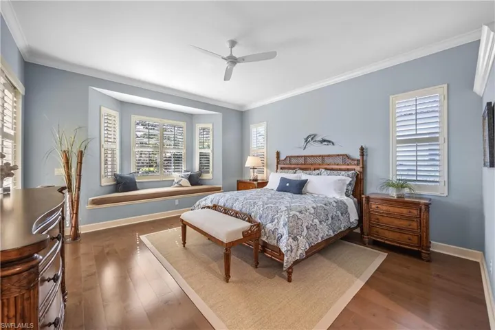 Bedroom with ceiling fan, dark wood-type flooring, and ornamental molding