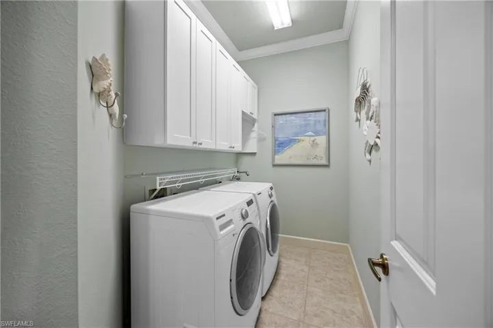 Laundry room with cabinets, washing machine and dryer, ornamental molding, and light tile patterned floors