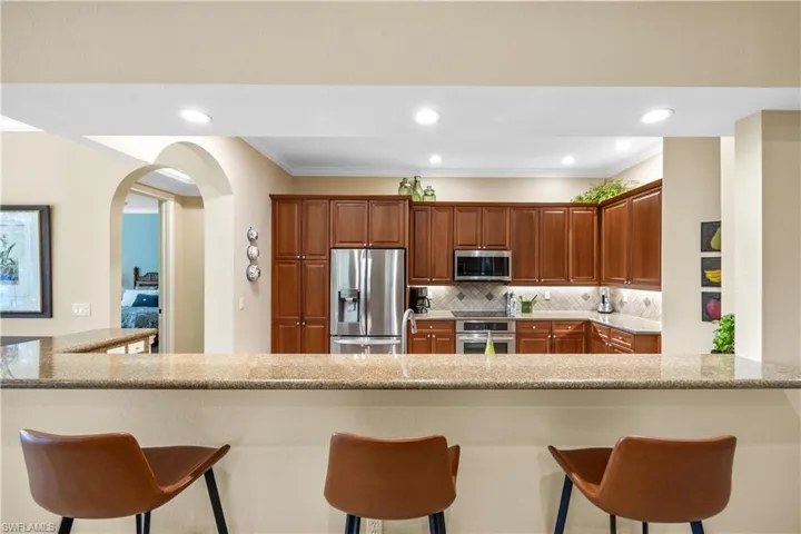 Kitchen with kitchen peninsula, light stone countertops, a breakfast bar, and appliances with stainless steel finishes