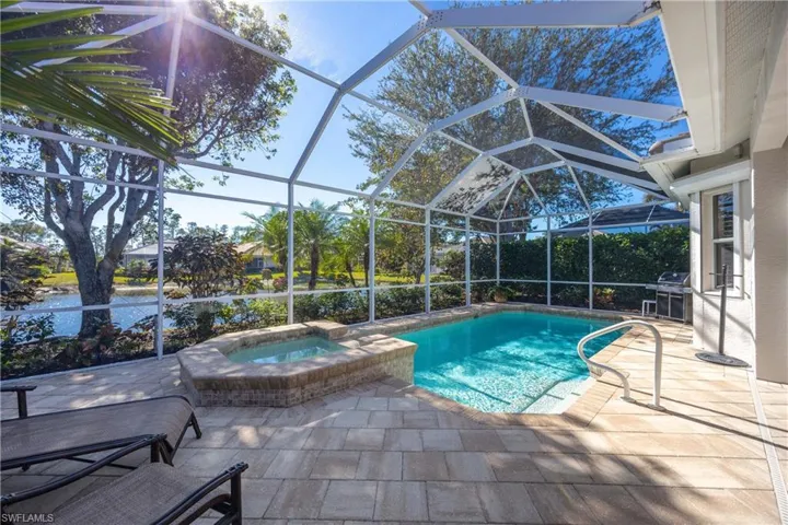 View of swimming pool with glass enclosure, a grill, a patio area, and an in ground hot tub