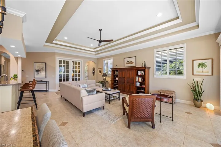 Tiled living room with french doors, ornamental molding, a tray ceiling, ceiling fan, and sink