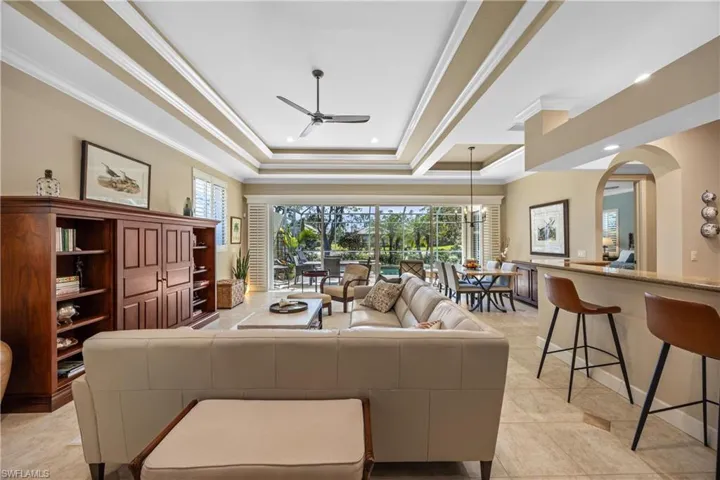 Tiled living room featuring a tray ceiling, crown molding, ceiling fan, and a healthy amount of sunlight