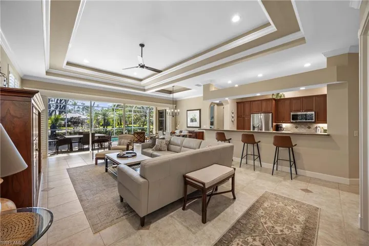 Living room with light tile patterned floors, ceiling fan with notable chandelier, a raised ceiling, and crown molding