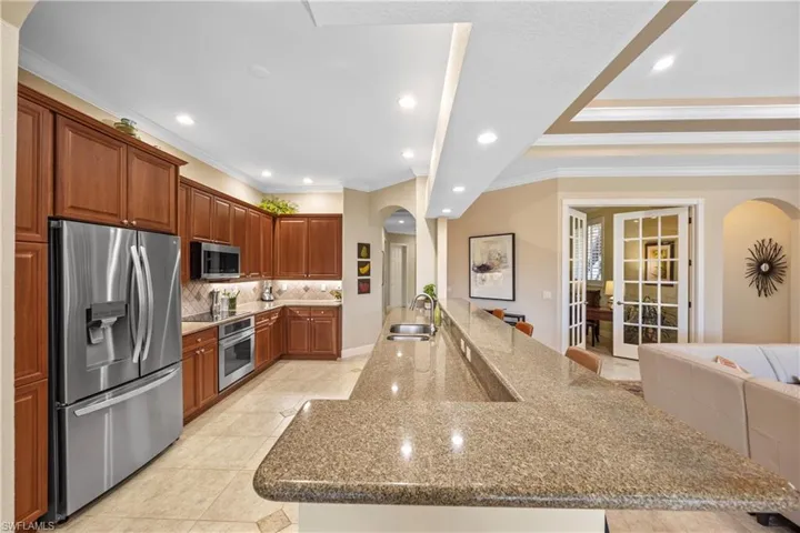 Kitchen with crown molding, sink, light stone countertops, appliances with stainless steel finishes, and light tile patterned flooring