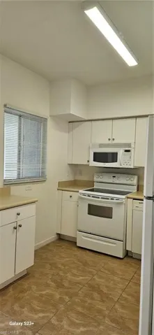 Kitchen with white cabinetry, stove, white microwave, light countertops, and fridge