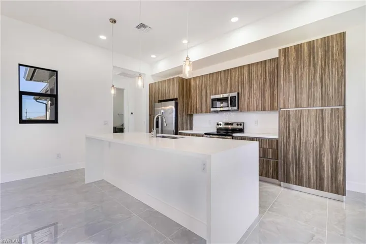 Kitchen with brown cabinets, light stone countertops, decorative light fixtures, a kitchen island with sink, and appliances with stainless steel finishes
