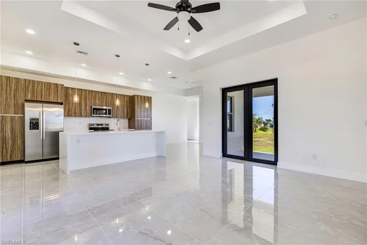Kitchen with a tray ceiling, an island with sink, modern cabinets, appliances with stainless steel finishes, and light marble finish floors