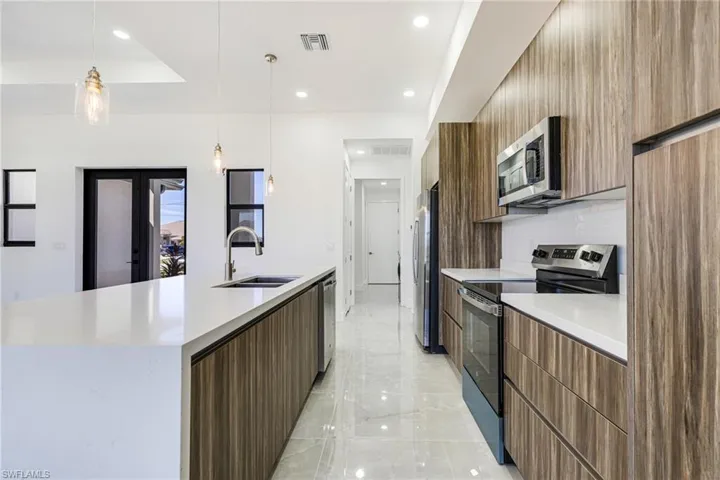 Kitchen featuring modern cabinets, appliances with stainless steel finishes, pendant lighting, light stone counters, and a large island