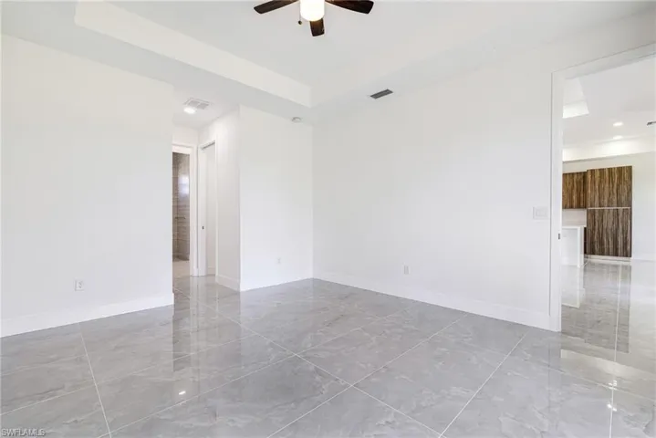 Empty room with a raised ceiling, a ceiling fan, and light marble finish flooring