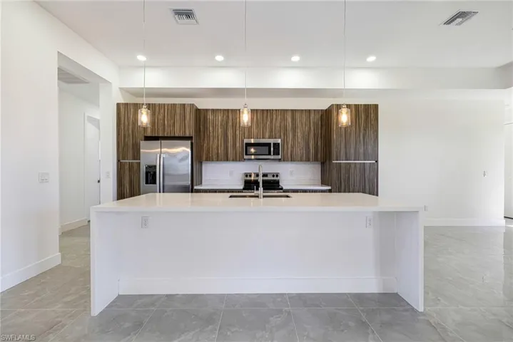 Kitchen with light stone counters, stainless steel appliances, modern cabinets, a large island with sink, and hanging light fixtures