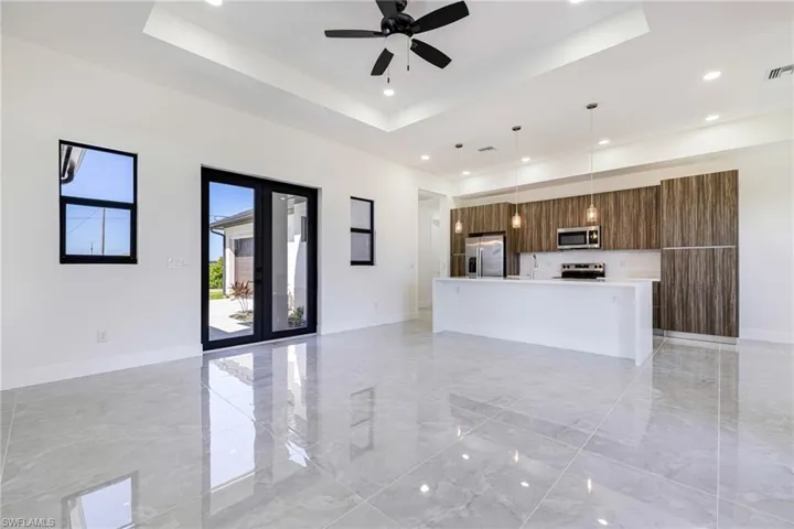 Unfurnished living room featuring a raised ceiling, light marble finish floors, recessed lighting, and ceiling fan