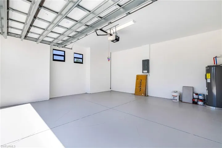 Garage with electric water heater, electric panel, and a garage door opener