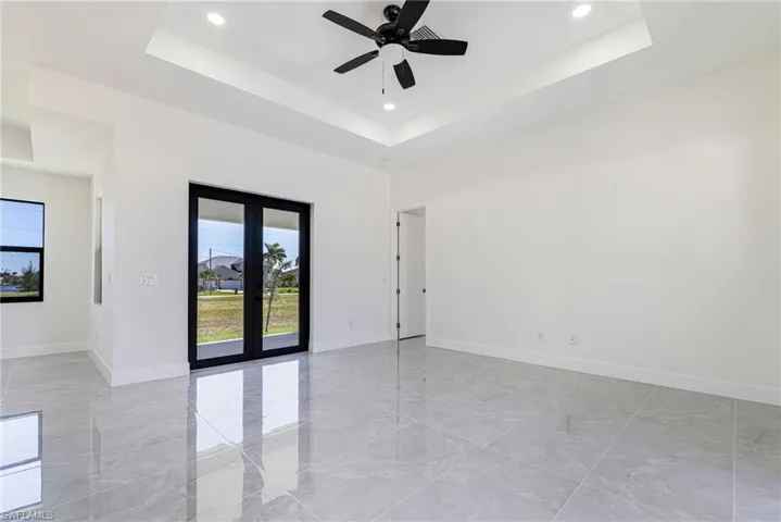 Spare room featuring a tray ceiling, french doors, light marble finish floors, and recessed lighting