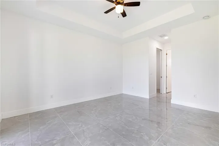 Empty room with a tray ceiling, a ceiling fan, and light marble finish floors