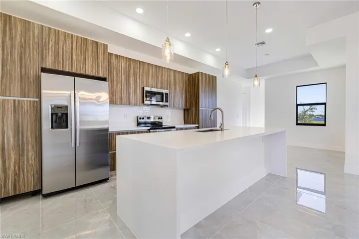 Kitchen featuring brown cabinets, appliances with stainless steel finishes, hanging light fixtures, light stone counters, and backsplash