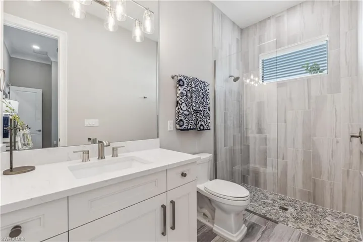 Bathroom with vanity, hardwood / wood-style flooring, toilet, ornamental molding, and tiled shower