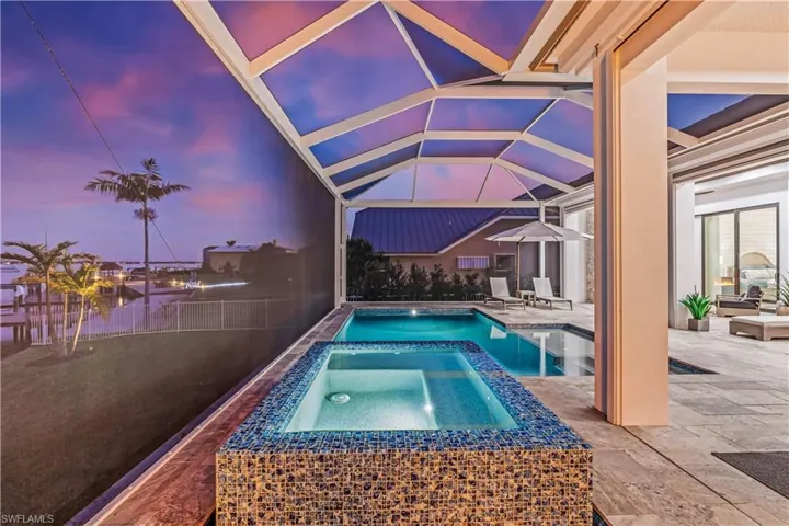 Pool at dusk featuring an in ground hot tub, a patio, and glass enclosure