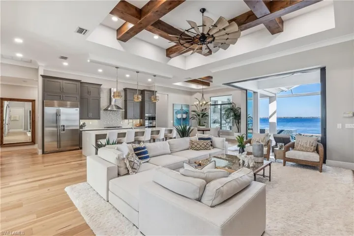 Living room with coffered ceiling, ceiling fan with notable chandelier, a water view, light wood-type flooring, and beam ceiling