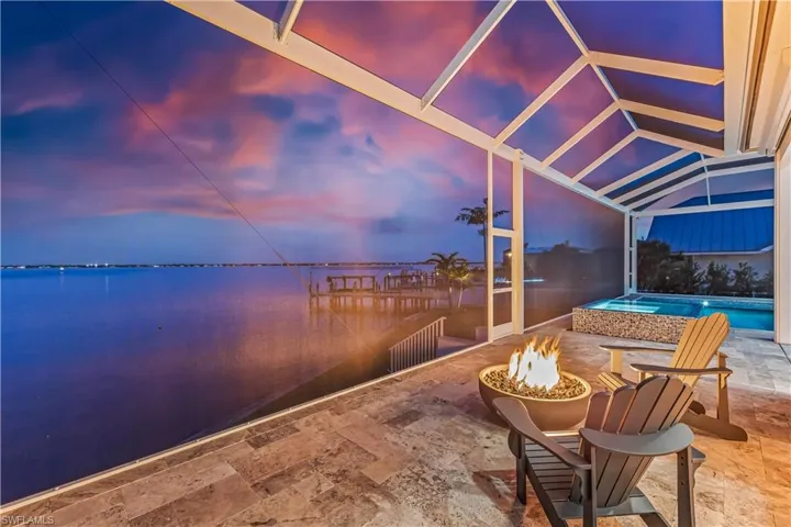 Patio terrace at dusk featuring a lanai, a swimming pool with hot tub, a water view, and an outdoor fire pit