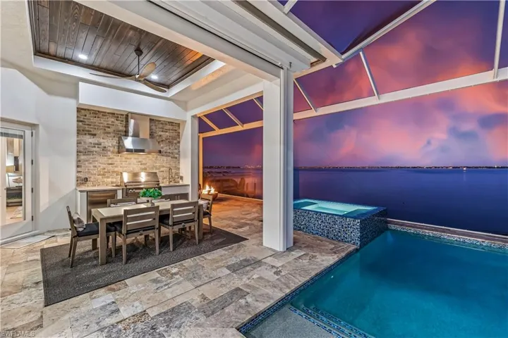 Patio terrace at dusk with a swimming pool with hot tub, an outdoor kitchen, a water view, and area for grilling