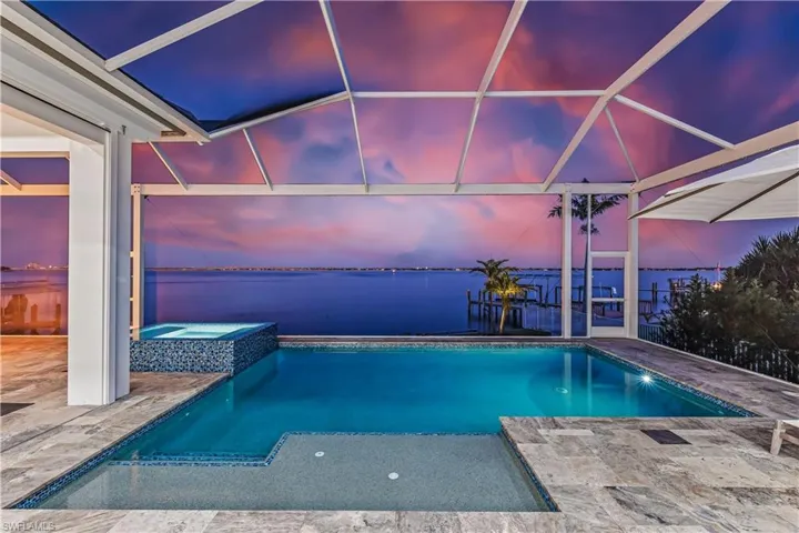 Pool at dusk with glass enclosure, an in ground hot tub, a water view, and a patio