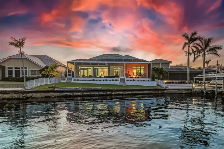 Back house at dusk with a yard, a water view, and a lanai