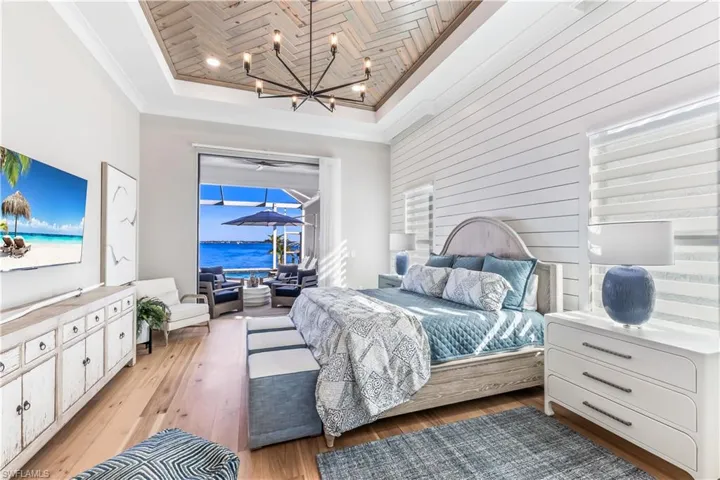 Master Bedroom featuring a towering ceiling, light wood-type flooring, a tray ceiling, a water view, and a chandelier