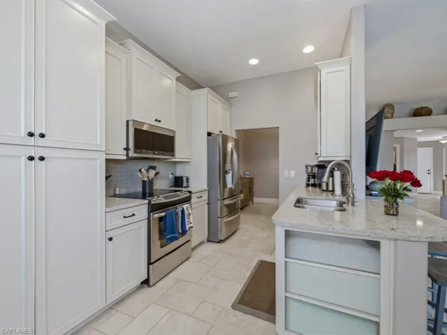 Kitchen featuring stainless steel appliances, light stone counters, white cabinetry, recessed lighting, and light stone finish flooring