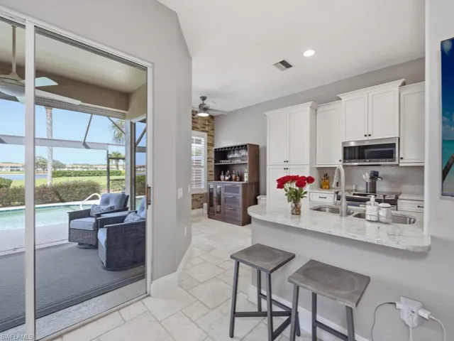 Kitchen featuring a kitchen bar, light stone counters, a ceiling fan, a sunroom, and stone tile flooring