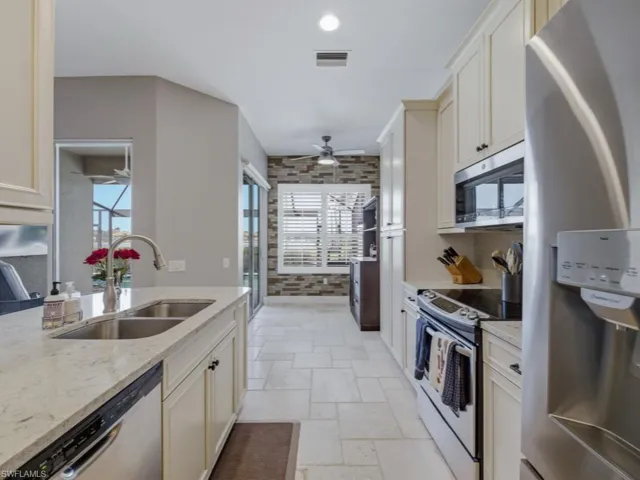 Kitchen with stainless steel appliances, stone tile floors, light stone countertops, ceiling fan, and brick wall