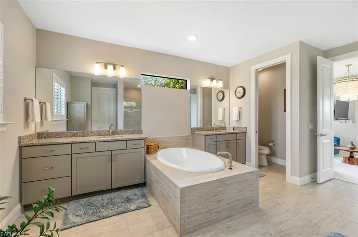 Bathroom with tiled bath, double vanity, tile patterned flooring, and a healthy amount of sunlight