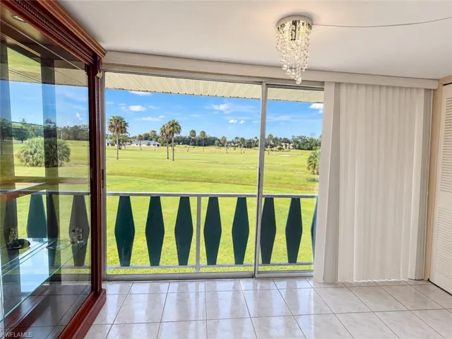 Sliding glass doors opening to a balcony with green decorative railing, tile flooring, and a crystal chandelier