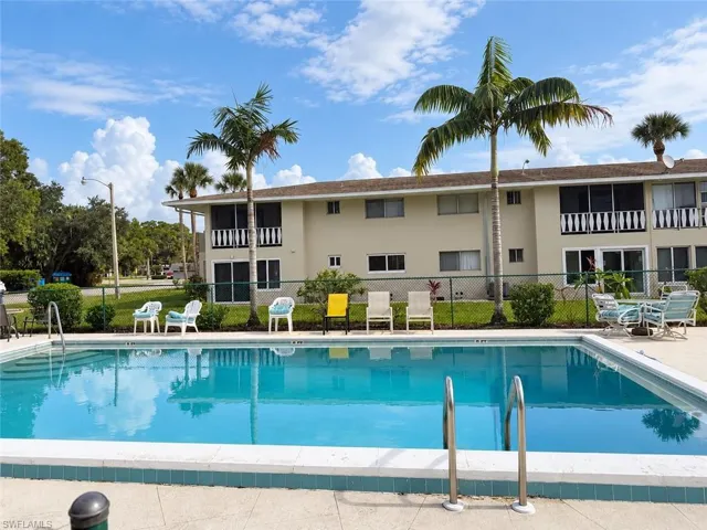 Community swimming pool with a concrete deck, metal handrails, and tropical landscaping