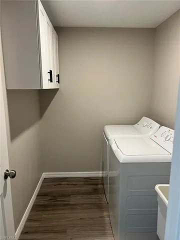 Laundry area featuring dark wood finished floors, washing machine and clothes dryer, and cabinet space