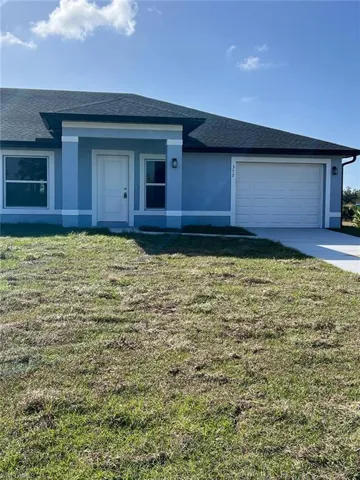 View of front facade featuring a shingled roof, a front yard, stucco siding, and a garage