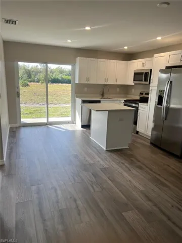 Kitchen with appliances with stainless steel finishes, recessed lighting, white cabinets, a kitchen island, and dark wood-style floors