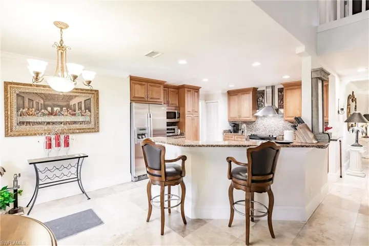 Kitchen with wall chimney exhaust hood, stainless steel appliances, stone counters, a breakfast bar area, and decorative backsplash