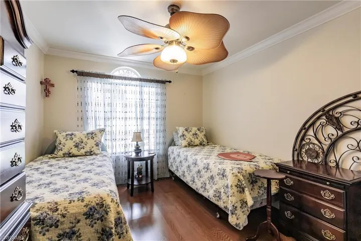 Bedroom with crown molding, dark wood-style floors, and a ceiling fan