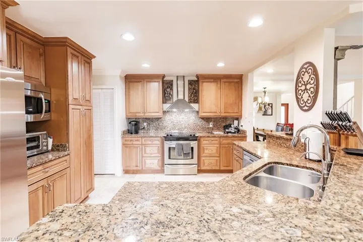 Kitchen featuring wall chimney exhaust hood, stainless steel appliances, light stone countertops, recessed lighting, and tasteful backsplash