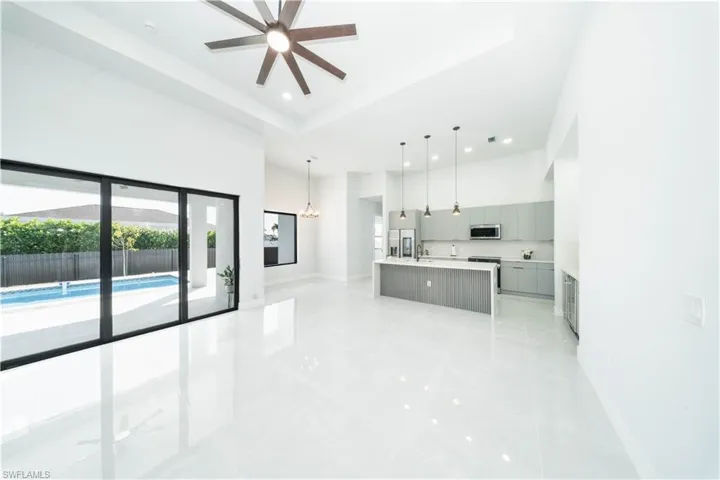Kitchen with a center island with sink, a - raised ceiling, gray cabinets, decorative light fixtures, and a ceiling fan