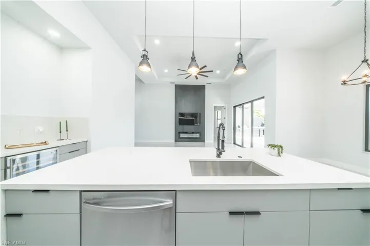 Kitchen featuring stainless steel l dishwasher, gray cabinetry, beverage cooler, pendant lighting, and a raised ceiling