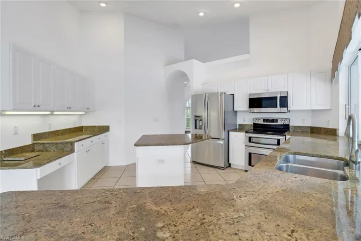 Kitchen with appliances with stainless steel finishes, white cabinetry, a towering ceiling, and a kitchen island
