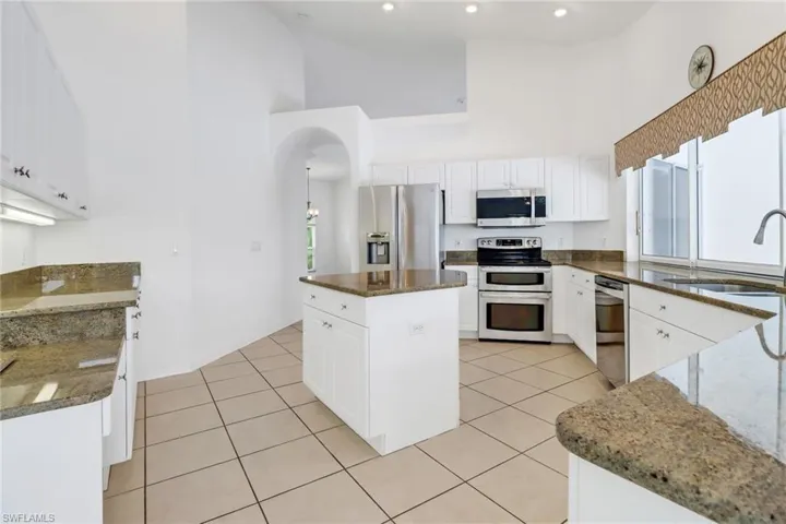 Kitchen with a high ceiling, white cabinets, a kitchen island, stainless steel appliances, and sink