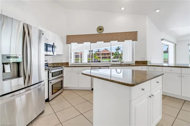 Kitchen featuring appliances with stainless steel finishes, white cabinets, dark stone countertops, and light tile patterned floors