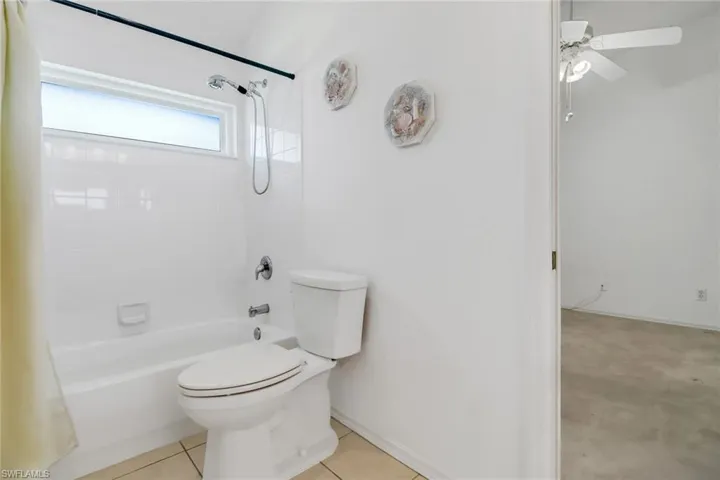 Bathroom featuring tiled shower / bath combo, toilet, ceiling fan, and tile patterned flooring