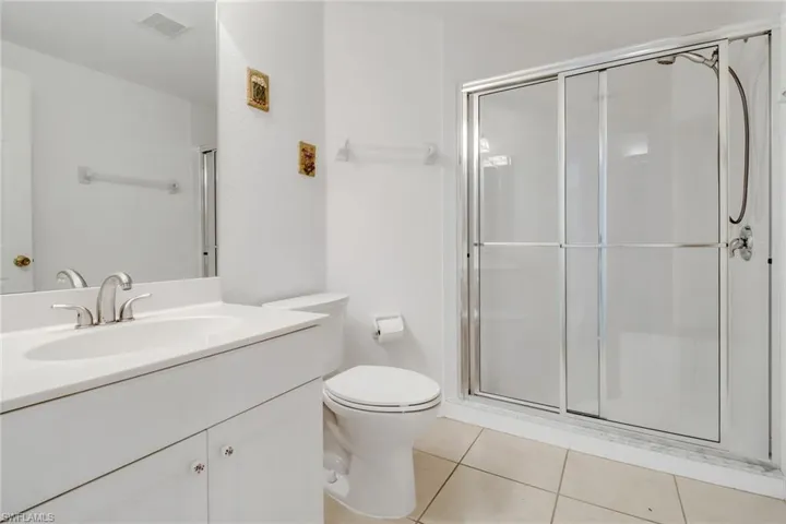 Bathroom with a shower with door, vanity, tile patterned flooring, and toilet