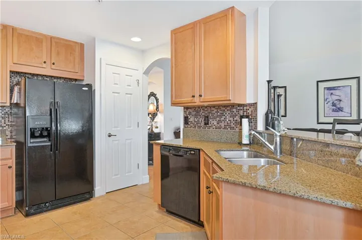 Kitchen featuring light wood cabinetry, granite countertops, a mosaic tile backsplash, and a double basin sink with a single-handle faucet