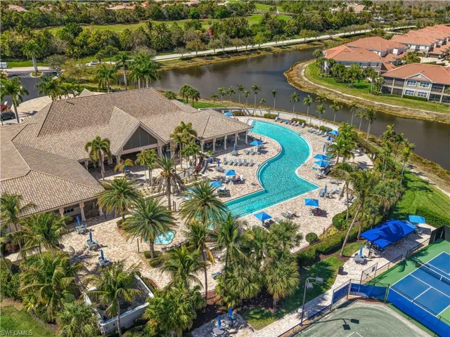 Community clubhouse featuring a large resort-style swimming pool, surrounding patio with lounge seating, multiple tennis courts, and lush tropical landscaping