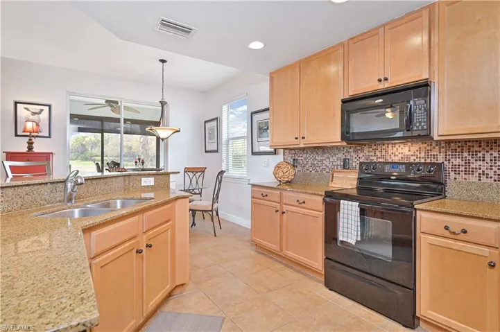 Spacious kitchen featuring light wood cabinetry, stone countertops, a mosaic tile backsplash, black appliances, and tile flooring